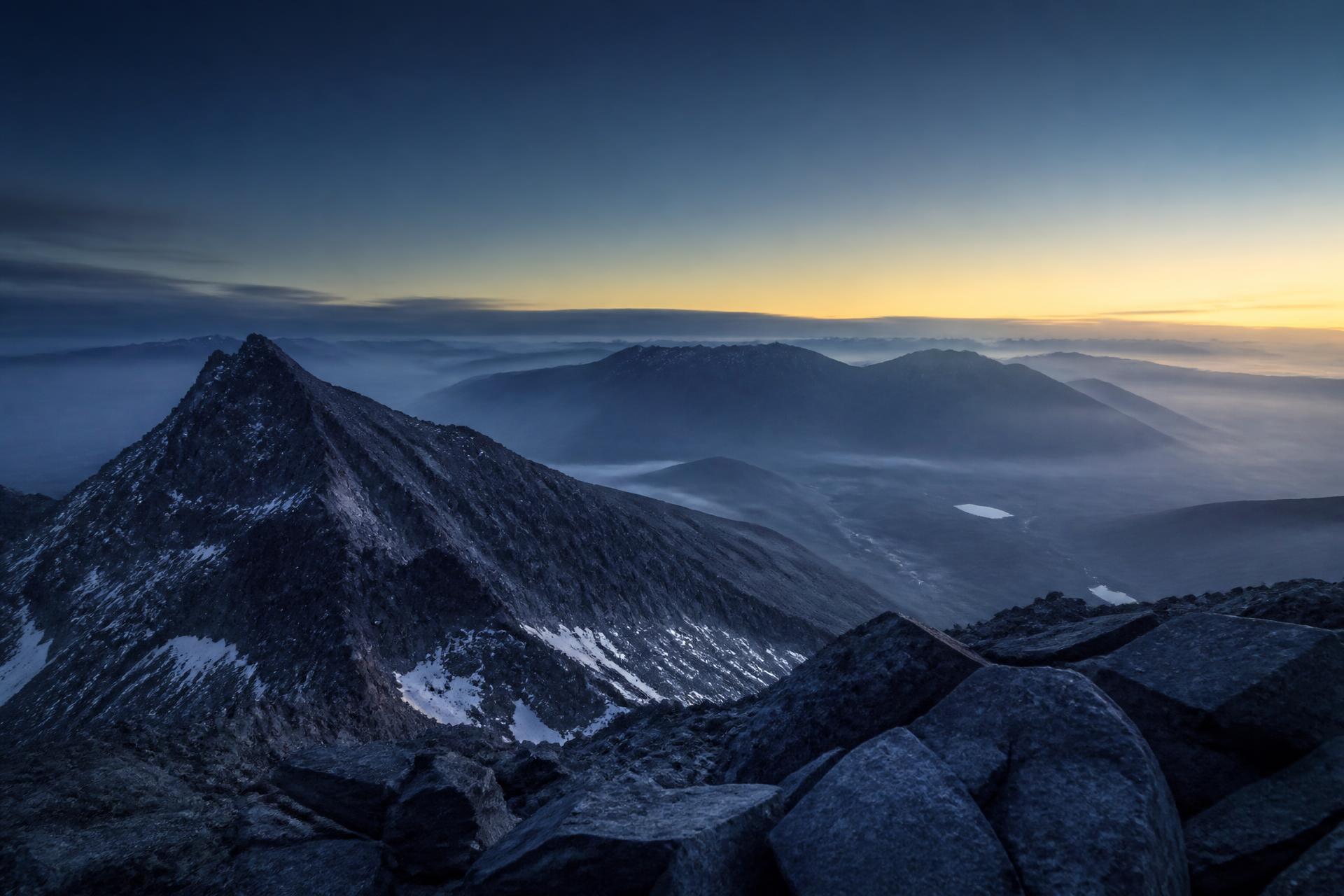 View from a mountain summit at dawn — layered peaks fading into mist